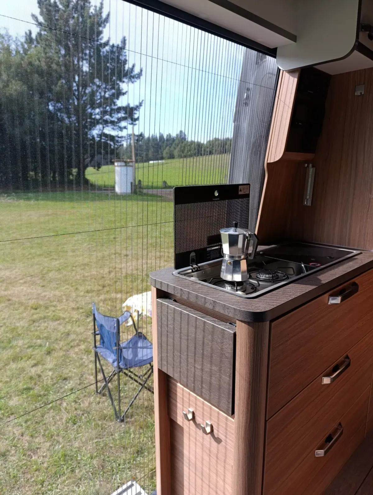 Vista desde el interior de la Camper Weinsberg Carabus 600 DQ de un campo y la zona de cocina